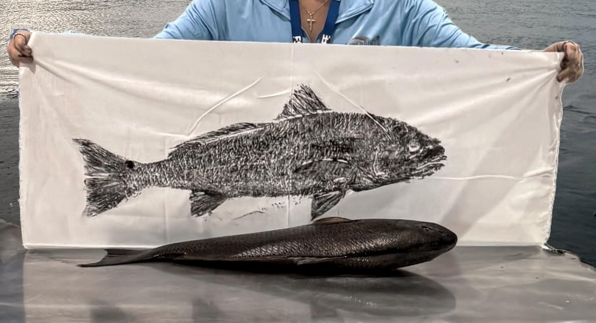 Angler holding gyotaku fish print of a redfish above the original fish on boat – custom catch-to-print fishing art on the water